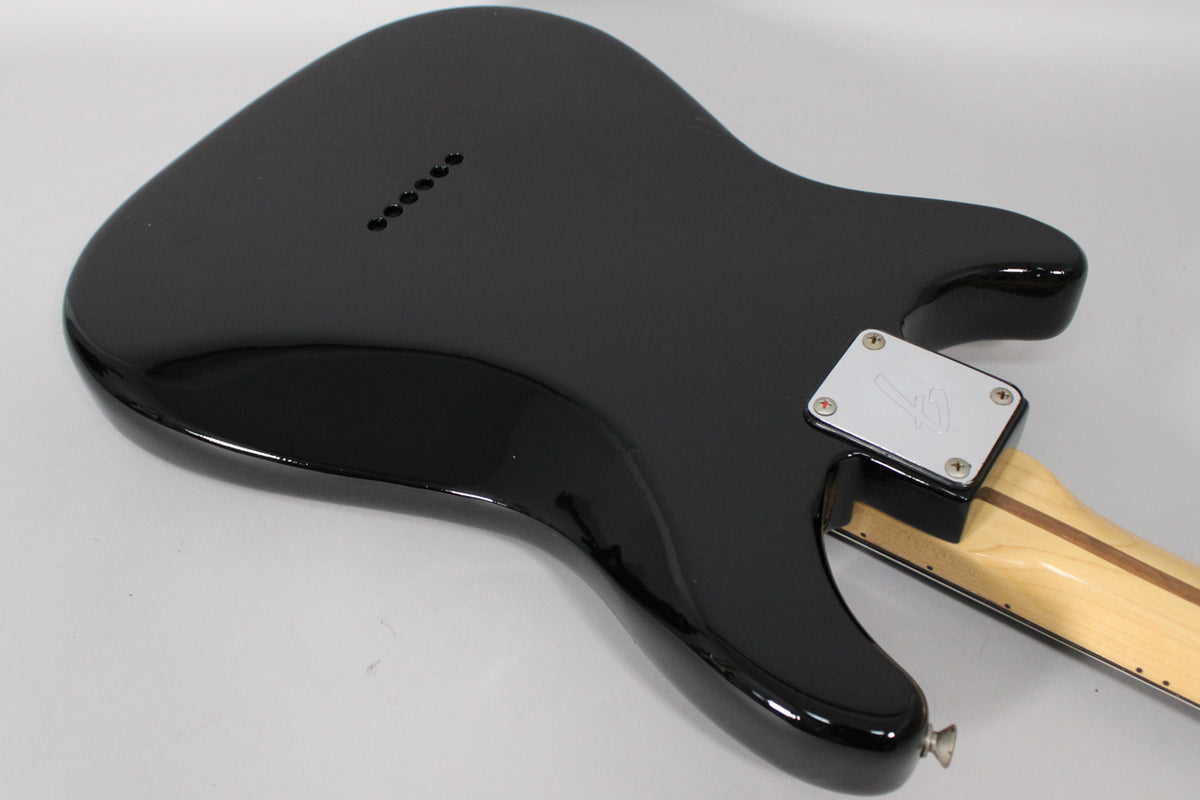 The guitar's glossy black body is seen from the back, angled to show the neck plate, strap button, and six string-through-body ferrules.