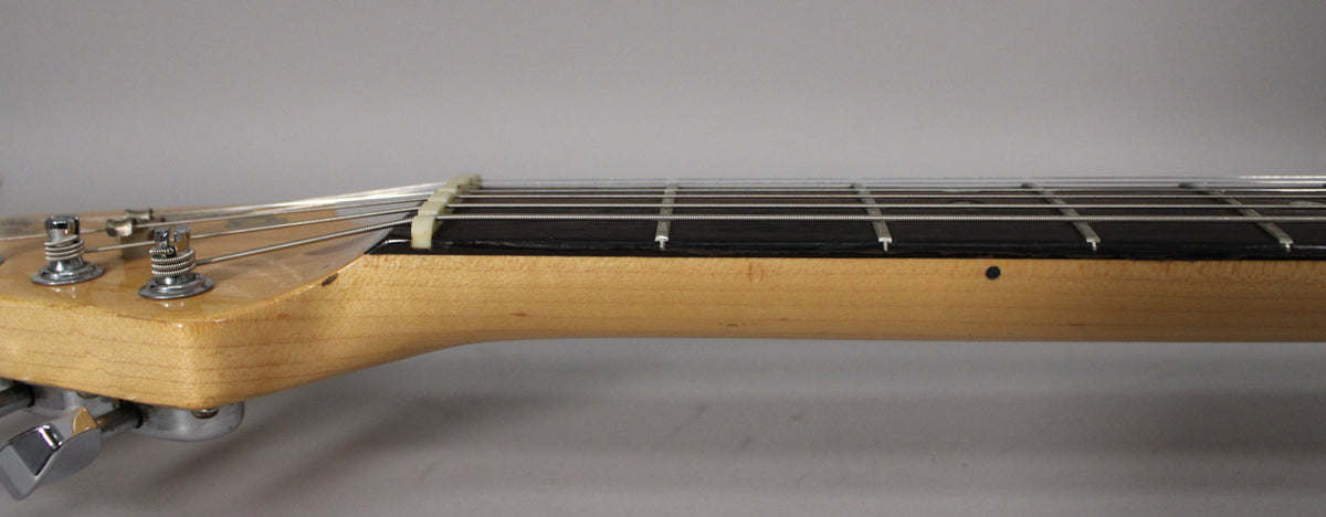 Close-up of the guitar neck and headstock from the side, showing the light wood finish, dark fretboard, and chrome tuners.