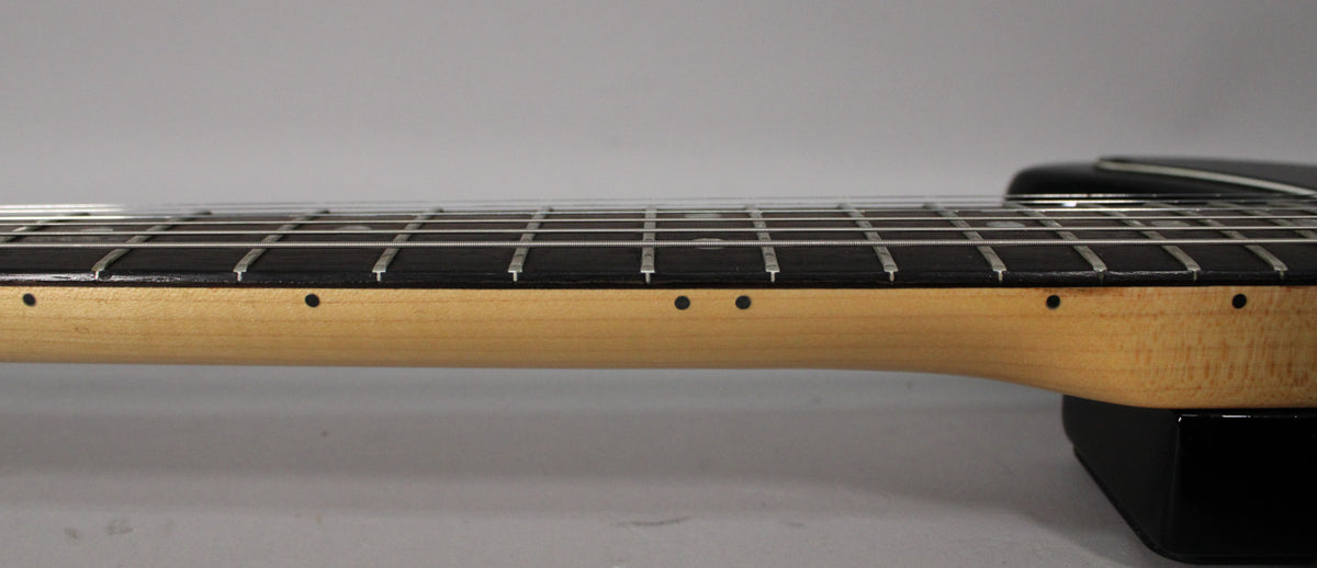 Side view of the guitar neck, showing a light wood neck, dark fretboard with dot inlays, and silver frets.