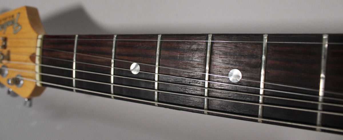 Close-up of the guitar's dark rosewood fretboard with six strings, silver frets, and two round, pearloid fret markers.