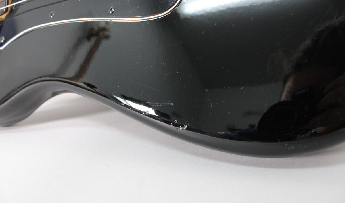 Close-up of the guitar's lower bout, showing a glossy black finish with numerous scratches and several chips along the edge.