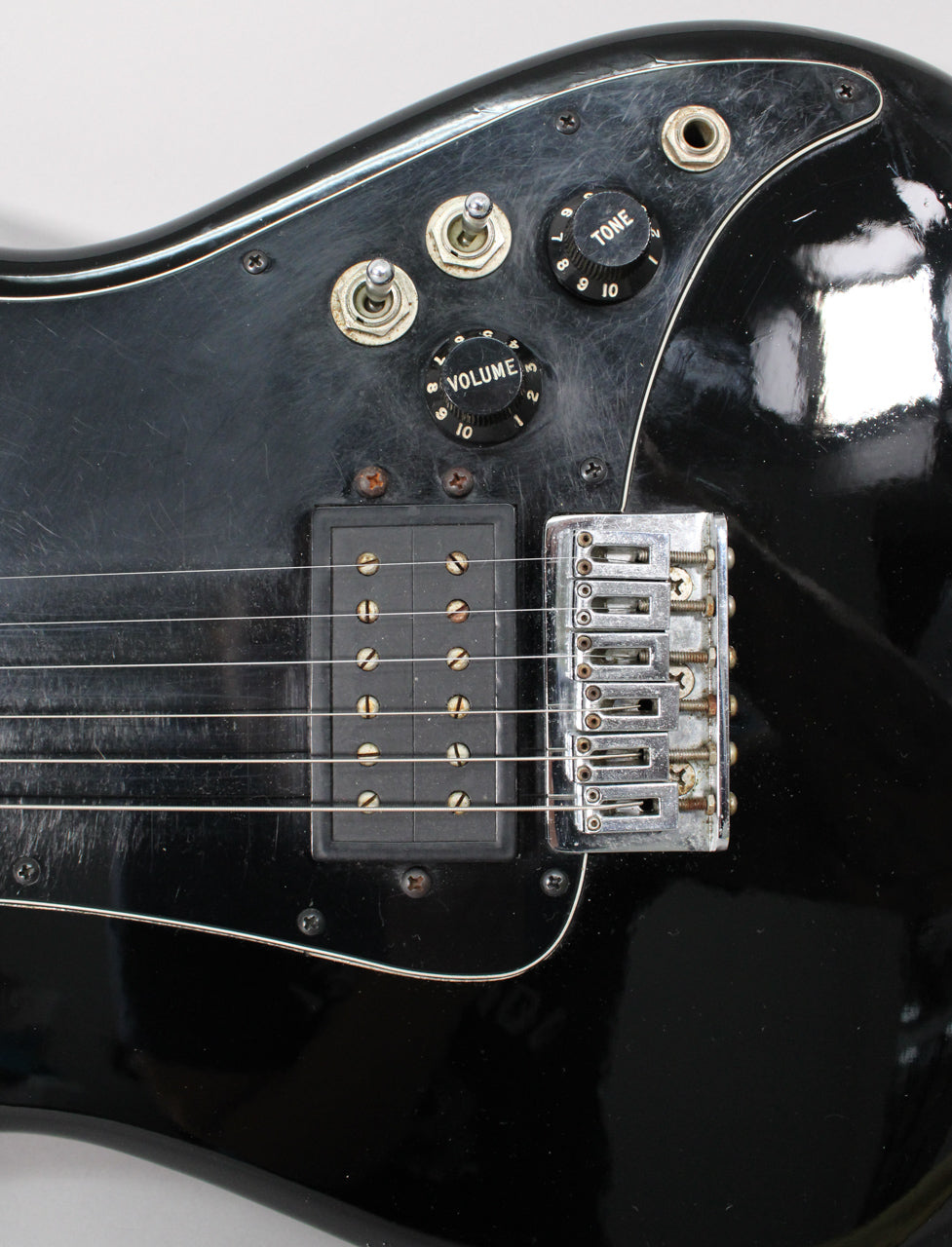 Close-up of the black guitar body, showing the bridge, humbucker pickup, two toggle switches, and volume and tone knobs, all with visible wear.