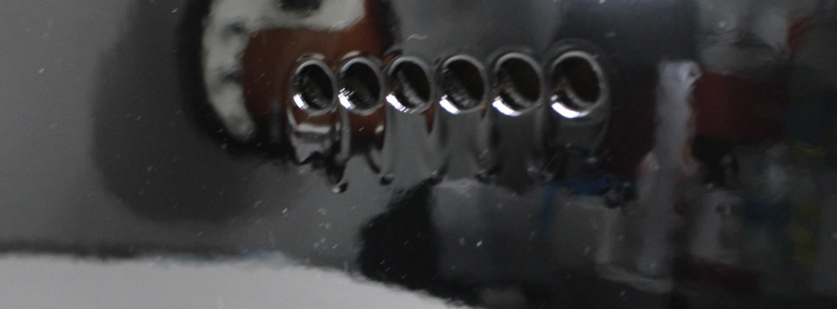 Close-up of the black guitar body, showing six chrome string ferrules on the back, with some dust and minor surface wear visible.