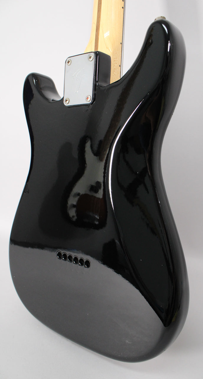The guitar's glossy black body is seen from the back, angled to the right, revealing a chrome neck plate and six string-through-body ferrules.