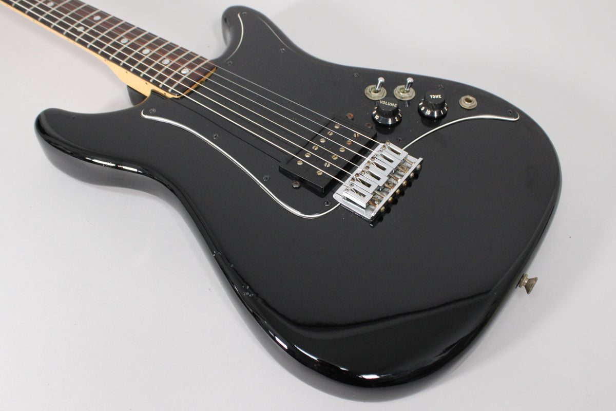 The black electric guitar is angled from the upper left, showing its glossy finish, single humbucker, chrome bridge, and two control knobs.