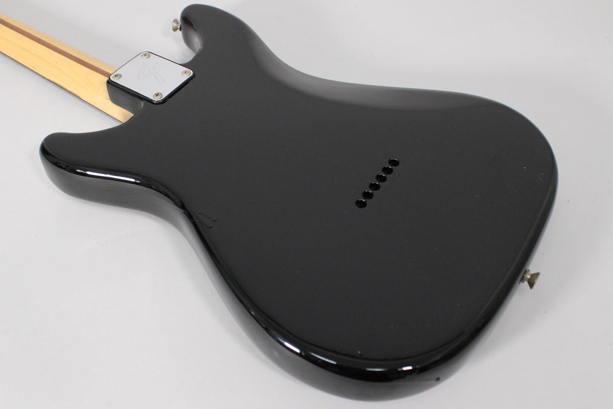 The black guitar body's back is angled, showing the neck plate, string-through-body ferrules, and a small ding on the lower bout.