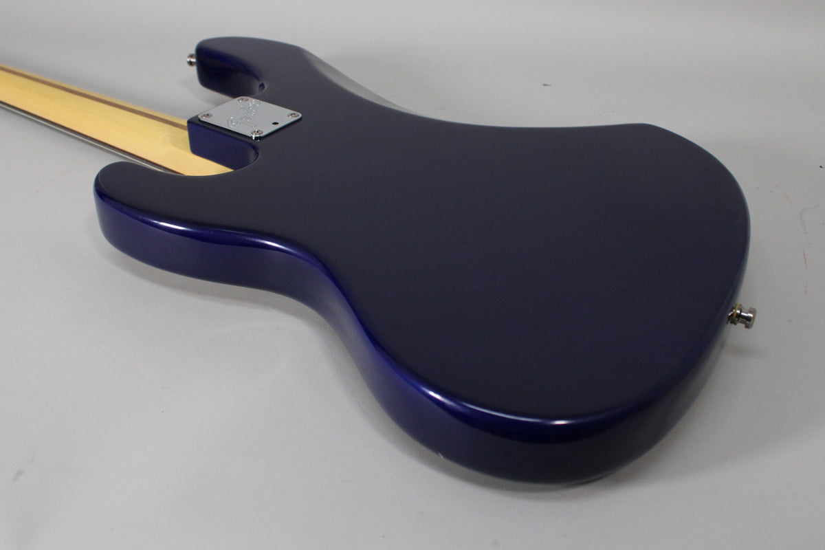 The bass guitar's midnight blue body is shown from the back, angled to reveal the maple neck and chrome neck plate.