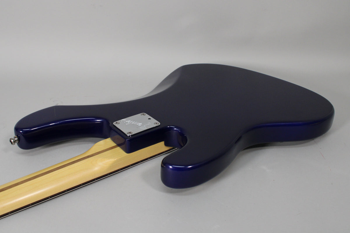 The midnight blue bass body, with a visible scratch on the upper horn, joins a light maple neck with dark wood stripes.