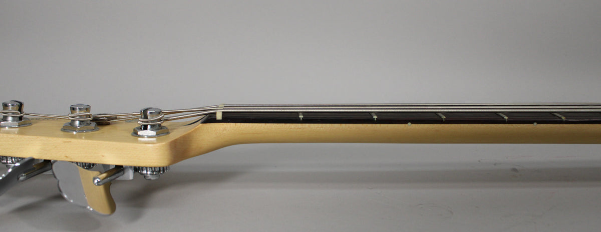 The bass headstock and neck are viewed from the side, showing the light wood neck, dark fretboard, and chrome tuning pegs.