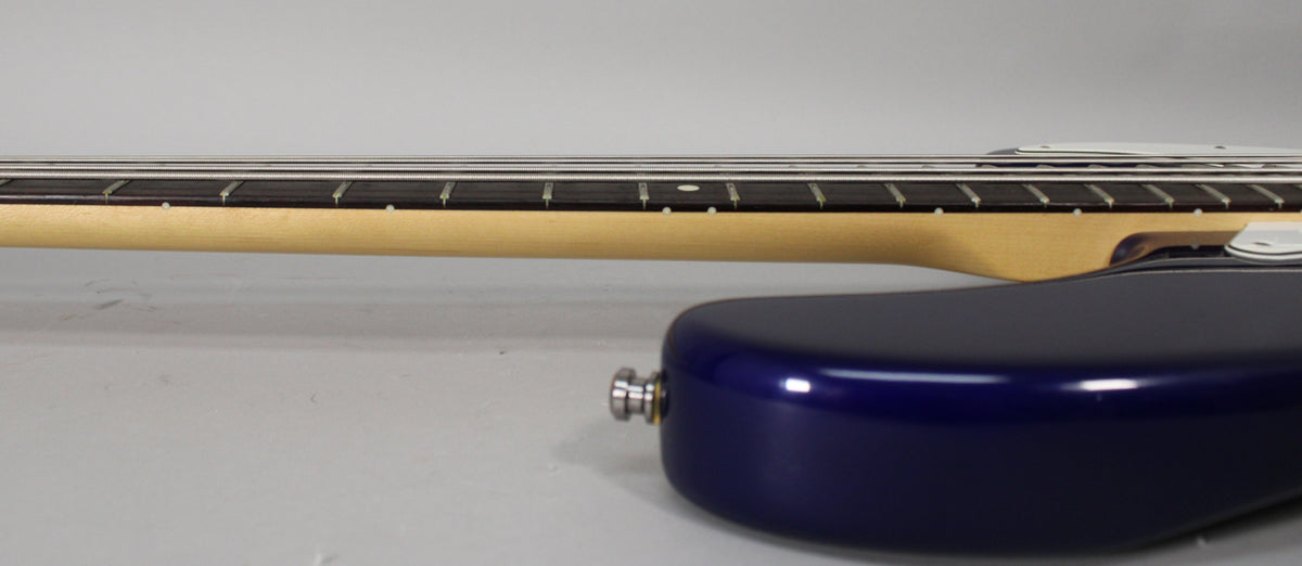 The bass guitar's midnight blue body and maple neck are seen from the side, with the fretboard and strings visible above.