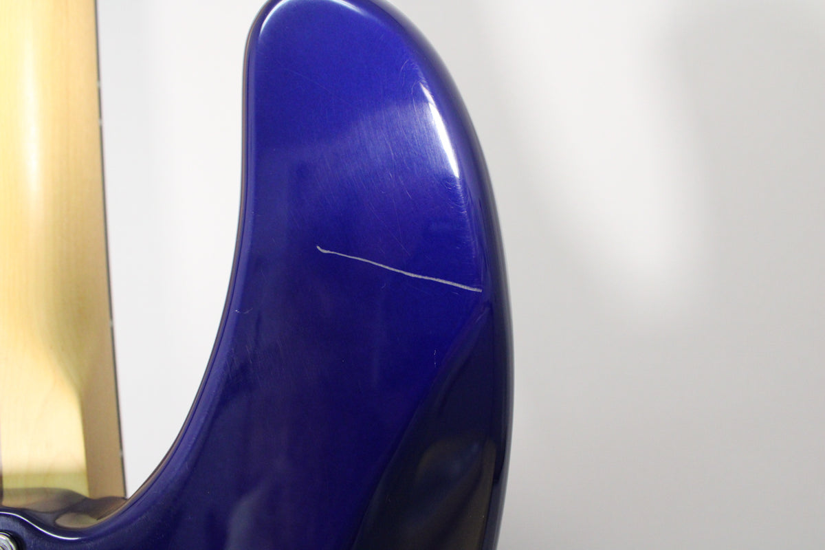Close-up of the bass's midnight blue body, showing a prominent horizontal scratch and many fine swirl marks on the glossy finish.