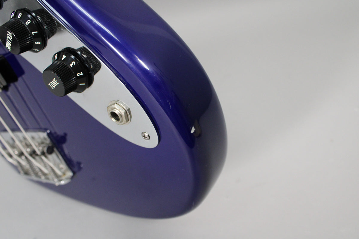Close-up of the bass's lower body, showing the input jack, two chrome control knobs, and a small chip on the midnight blue finish.