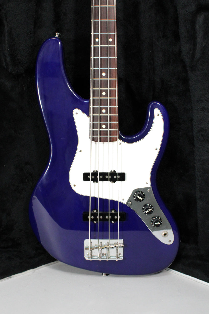 A full-front view of a glossy midnight blue bass with a white pickguard, two black pickups, and three chrome control knobs.