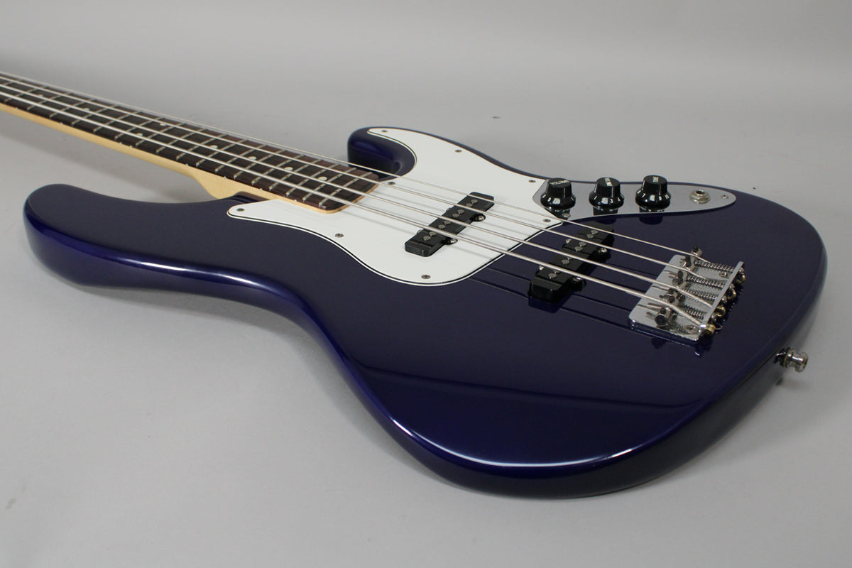 The midnight blue bass body with a white pickguard is angled, showing the chrome bridge, three black control knobs, and neck.
