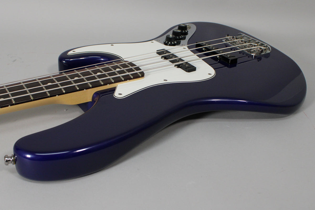 The midnight blue bass body is angled from the lower left, showing the white pickguard, two pickups, and chrome bridge.