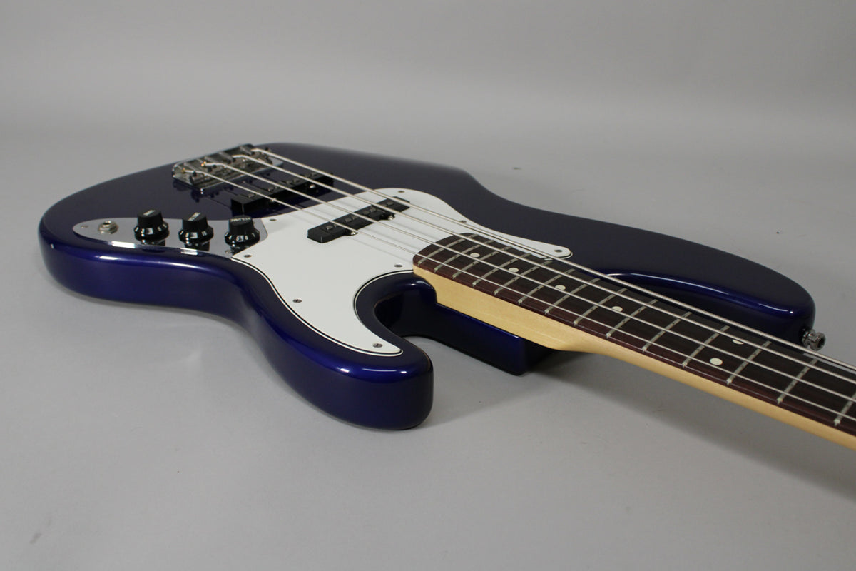 A midnight blue bass, angled right, showing the body, white pickguard, three black control knobs, and rosewood fretboard.