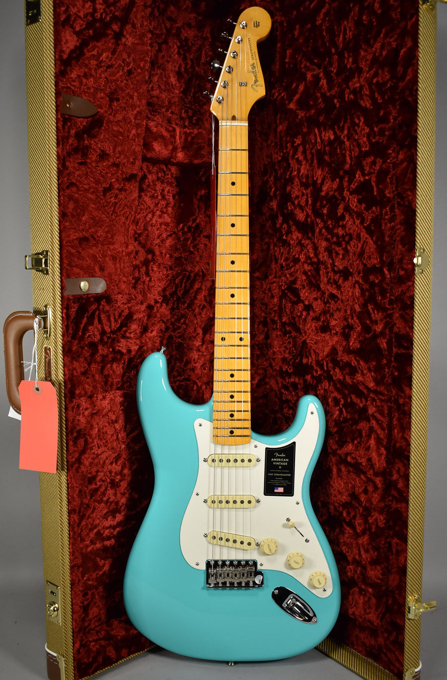 Full-length view of a glossy seafoam green Stratocaster with a maple neck, white pickguard, and cream knobs, in a tweed case with red velvet lining.