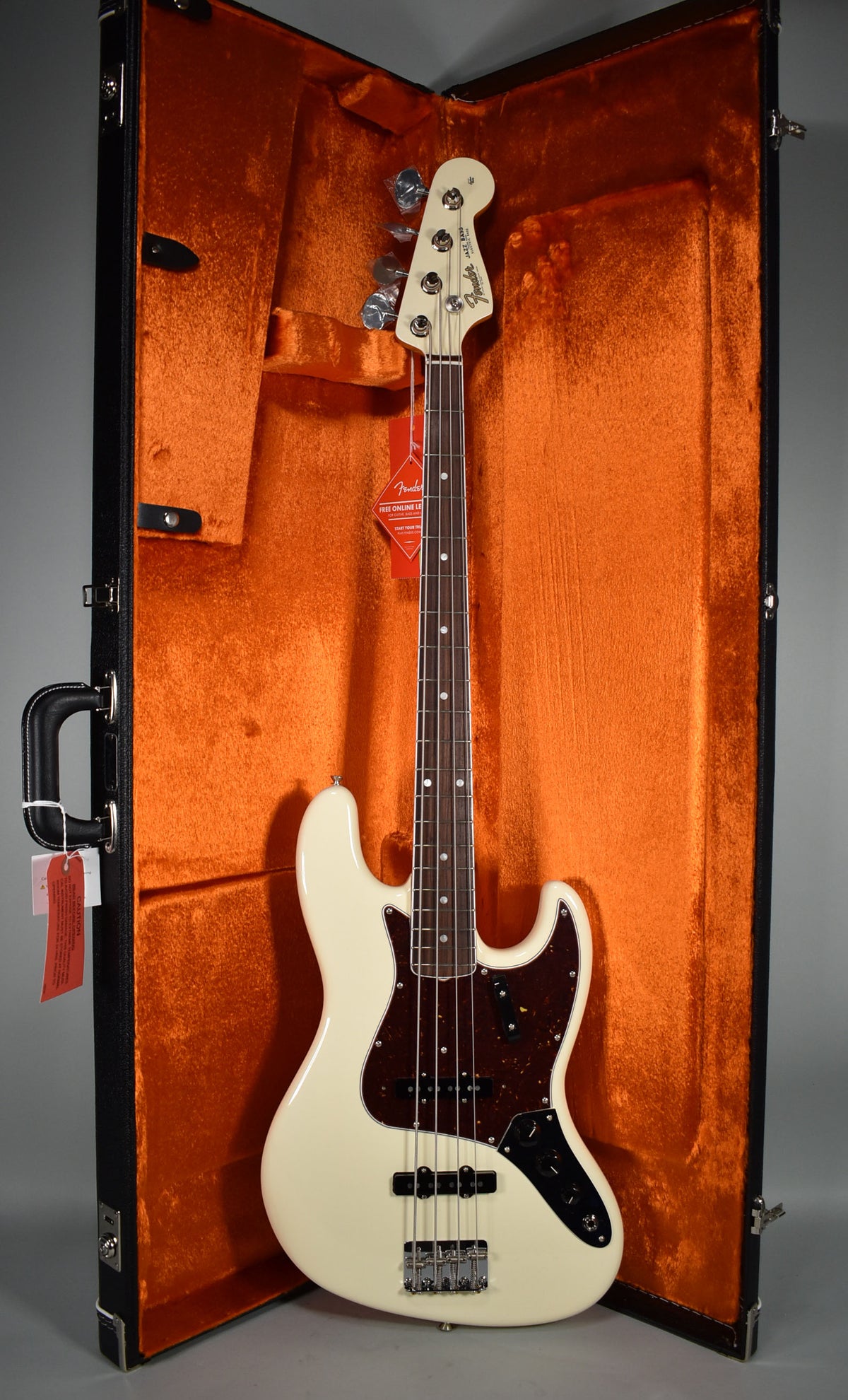 Full view of an Olympic White bass with a tortoiseshell pickguard, resting in an open hard case with orange plush lining.