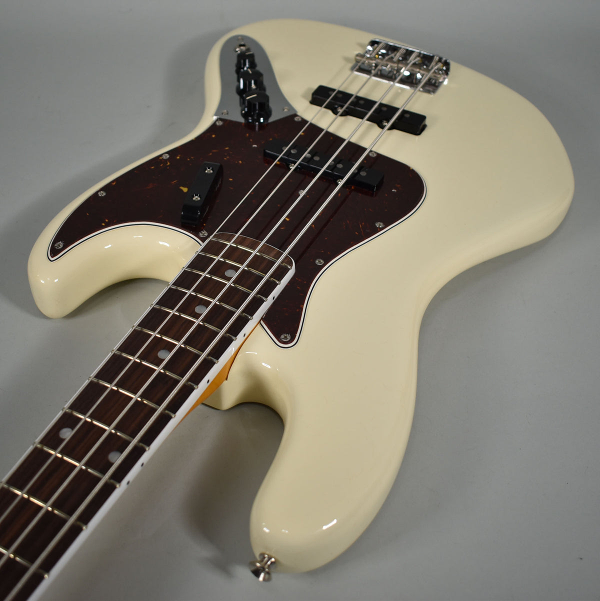 An Olympic White bass, angled from the neck, showing the body, tortoiseshell pickguard, and chrome bridge.