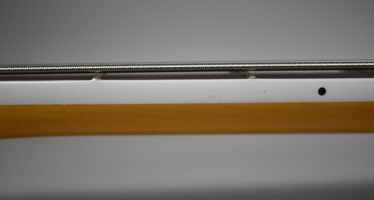 Close-up of the bass neck from the side, showing the light wood, white binding, and a black dot marker.