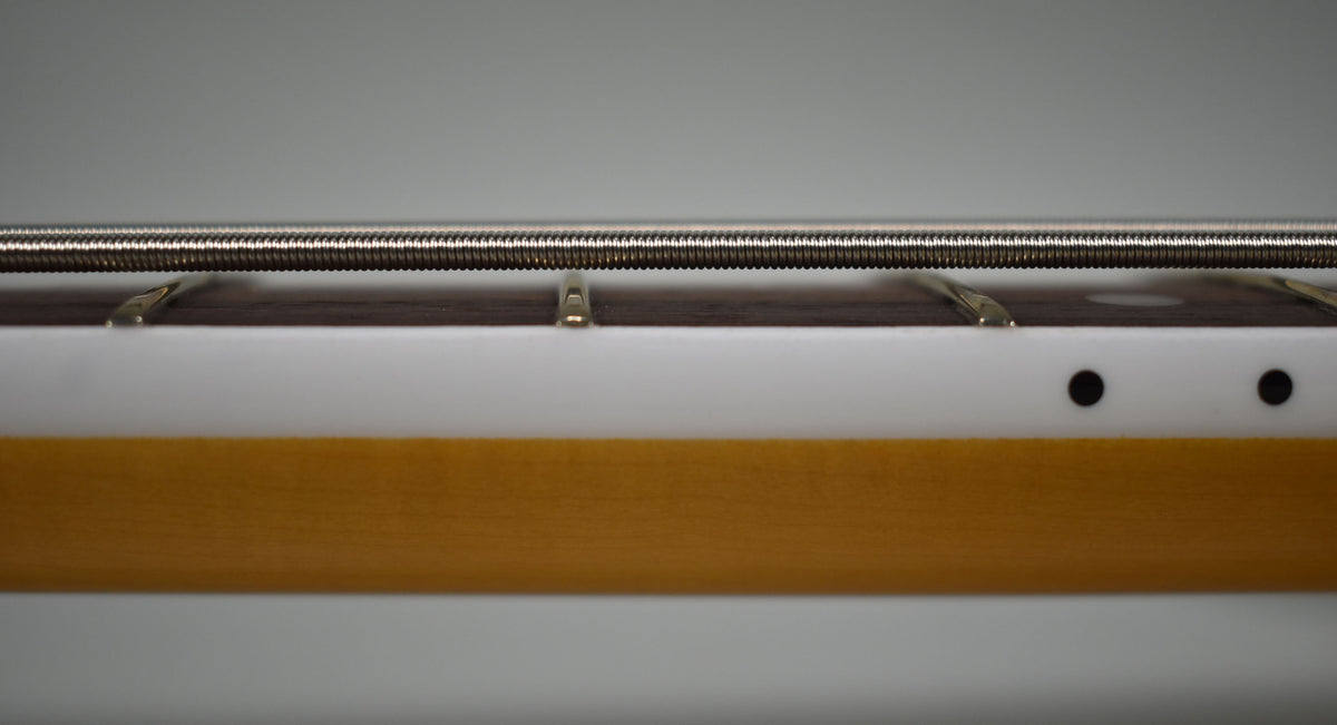 Close-up of the bass neck from the side, showing the dark fretboard, white binding, and two black side dots on the maple neck.
