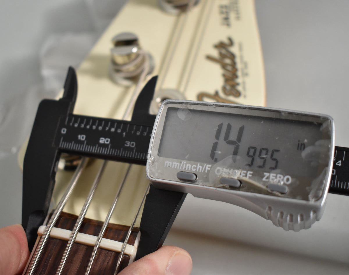 A digital caliper measures the bass's nut width at 1.4995 inches, with a dark rosewood fretboard and cream-colored nut visible.