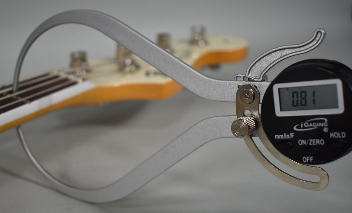 A digital caliper measures string height at the first fret of the Olympic White Jazz Bass, showing 0.81mm.