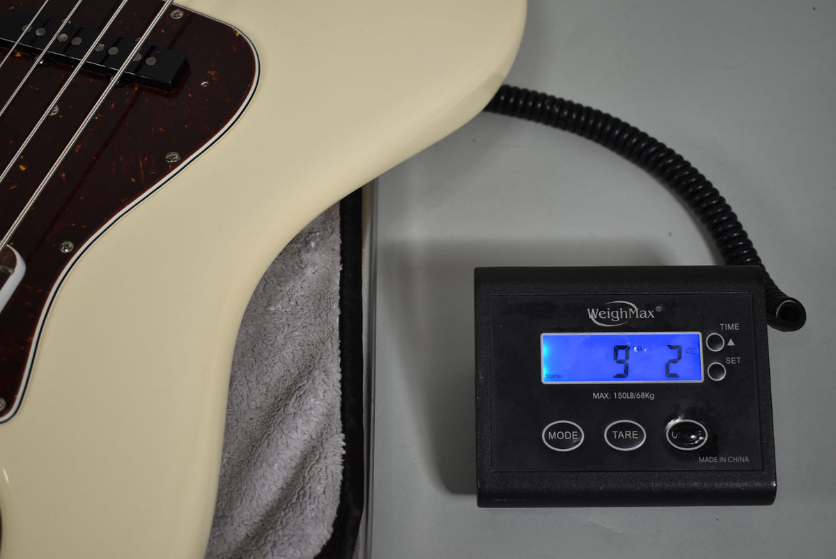 The Olympic White Jazz Bass body is shown on a scale displaying "9.2" lbs, with its tortoiseshell pickguard and pickups visible.