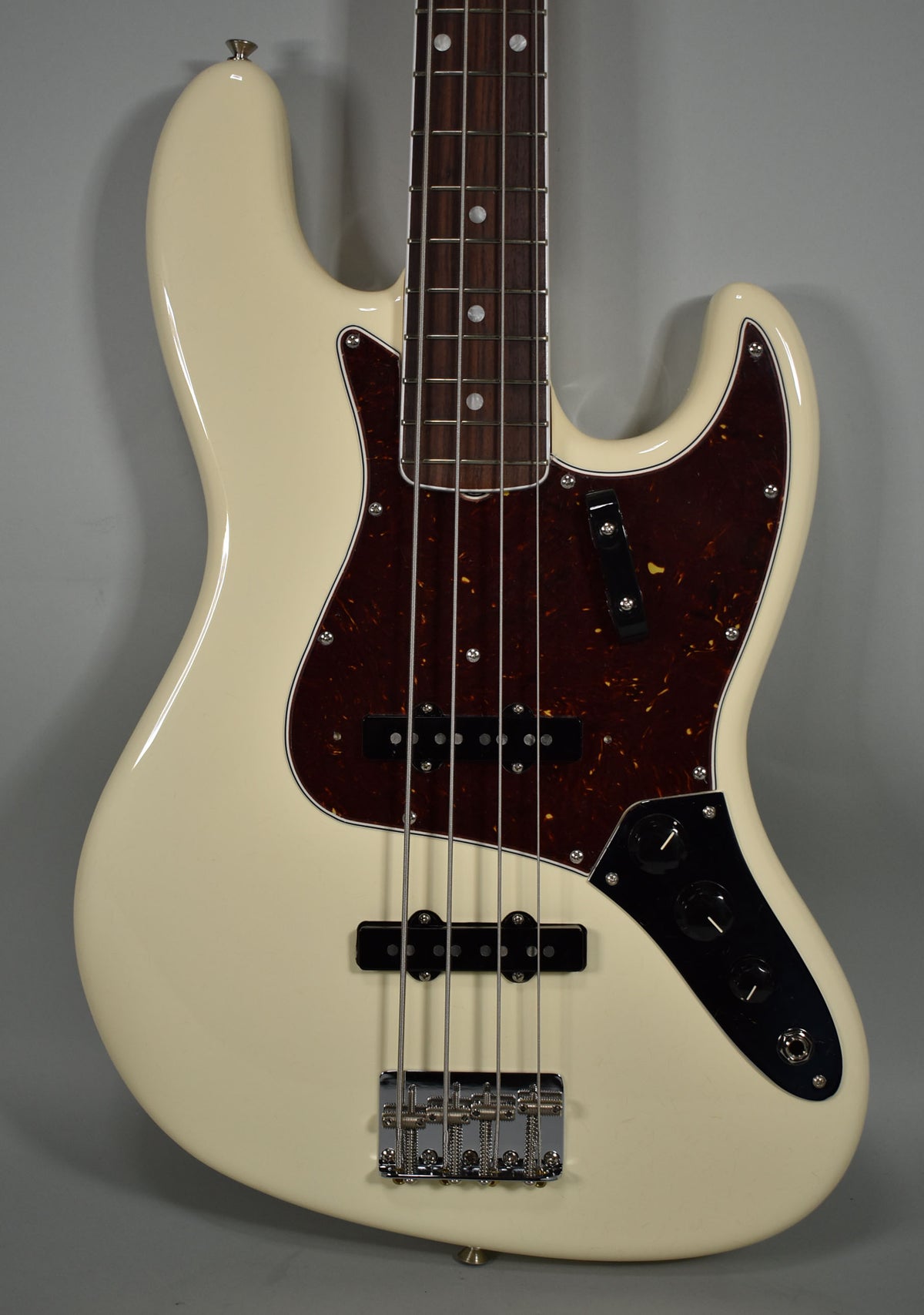 Full view of an Olympic White bass with a tortoiseshell pickguard, two black single-coil pickups, and three black control knobs.
