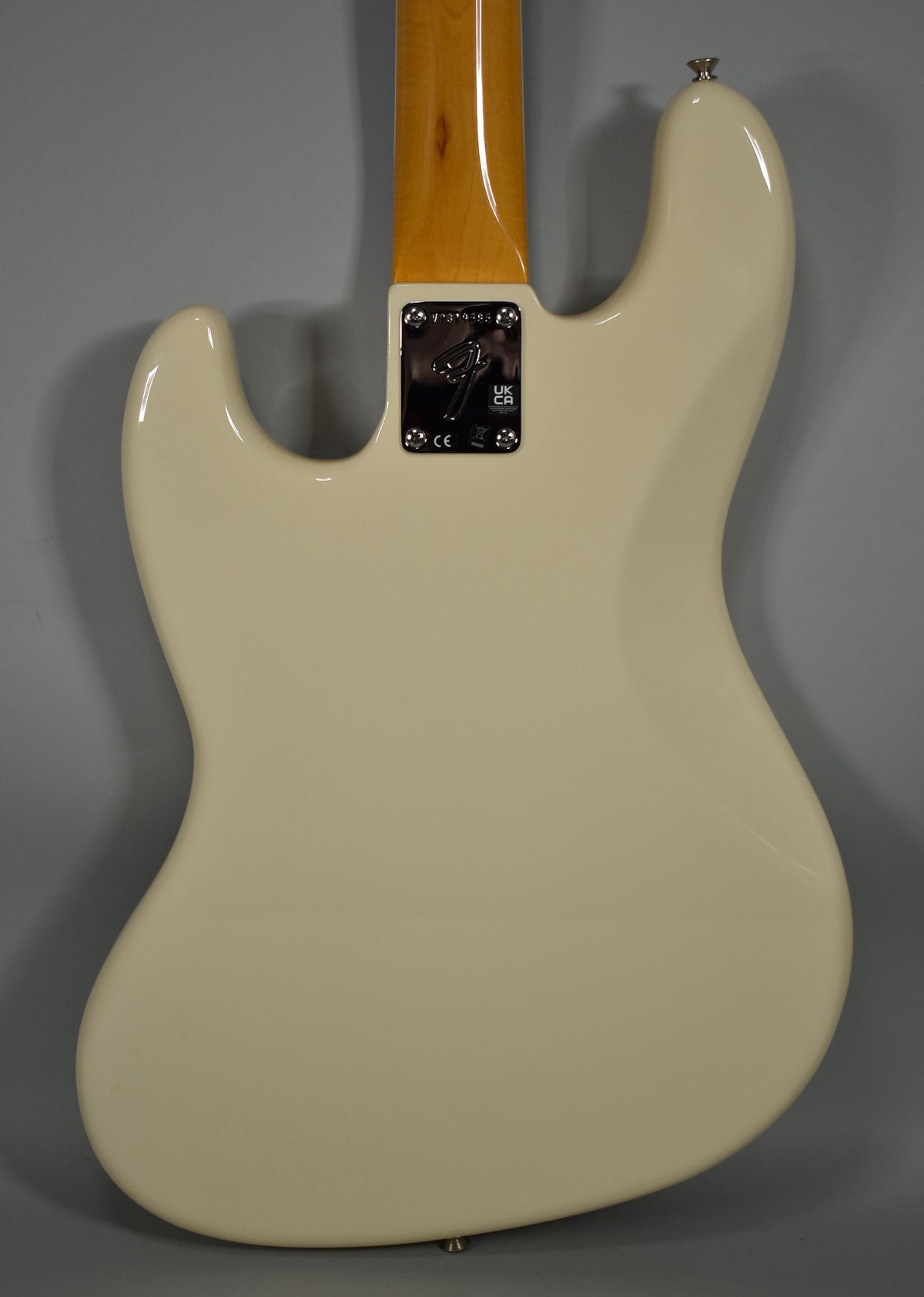 The back of an Olympic White bass, showing the neck plate, a light maple neck, and a strap button.