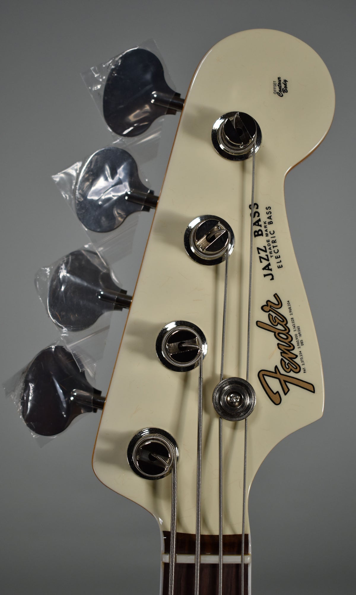 Close-up of the bass headstock, Olympic White with a glossy finish, showing chrome tuners, three still in plastic.
