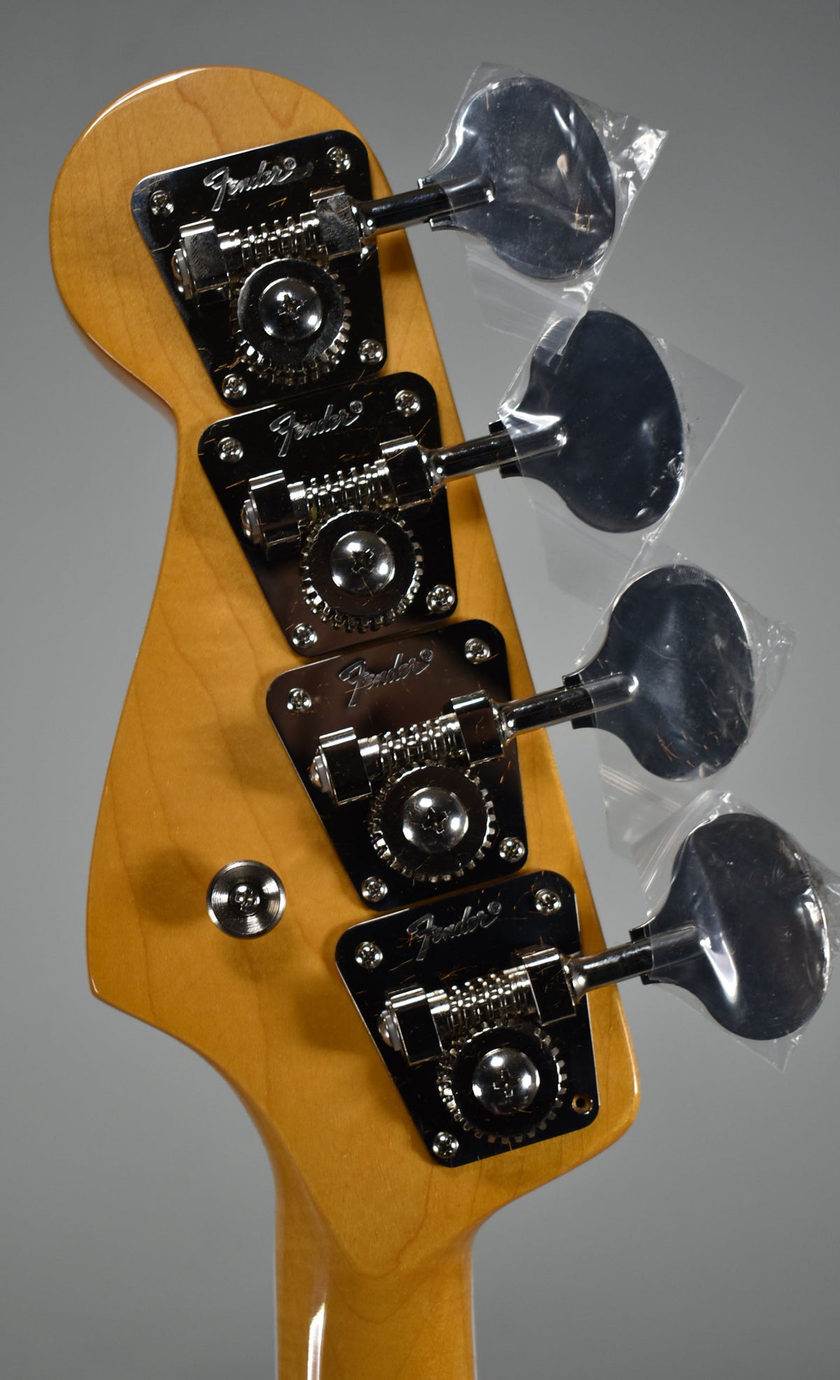 Close-up of the bass headstock, showing four chrome tuning machines with their paddles still in protective plastic.