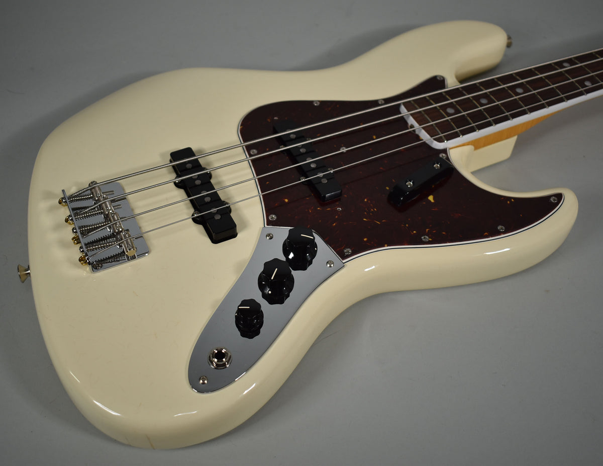 Upper body of an Olympic White bass, showing a tortoiseshell pickguard, chrome bridge, and control plate with black knobs.