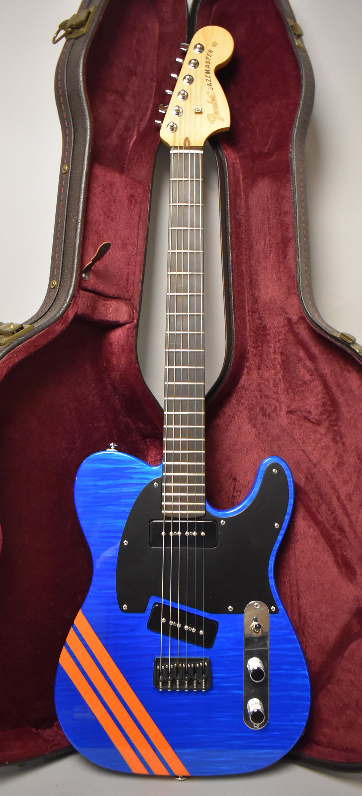 Full-length view of a blue flame-top guitar with orange racing stripes, black pickguard, two P-90 pickups, and a maple neck.