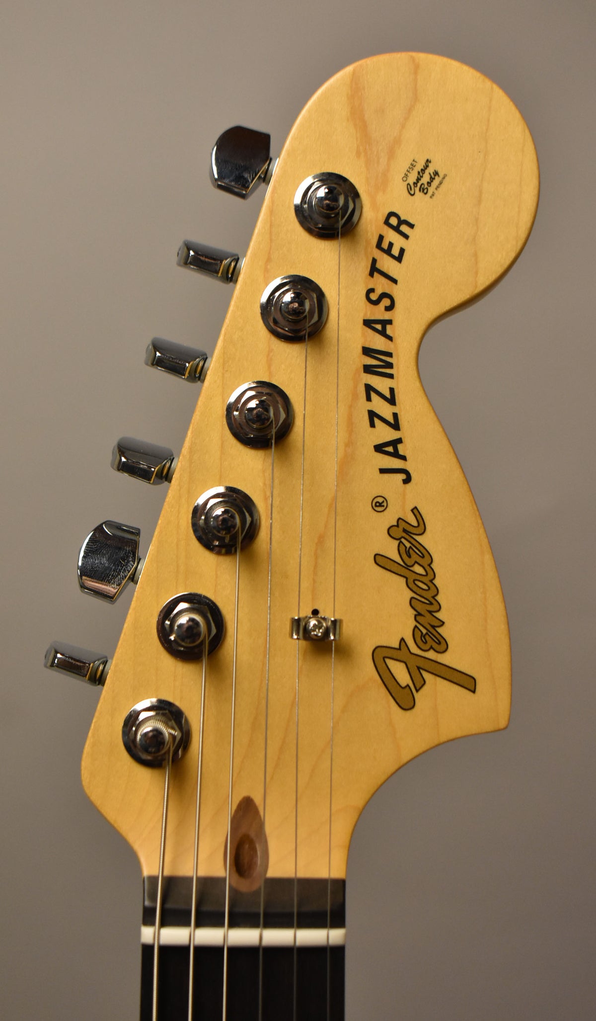 Close-up of a light maple headstock with six chrome tuners, a string tree, and a dark wood string retainer.