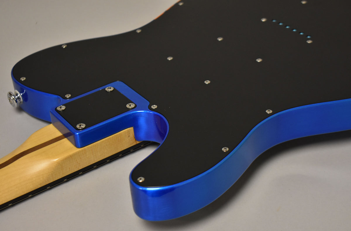 The guitar's back, showing the metallic blue body, black backplate with screws, and the natural wood neck joint.