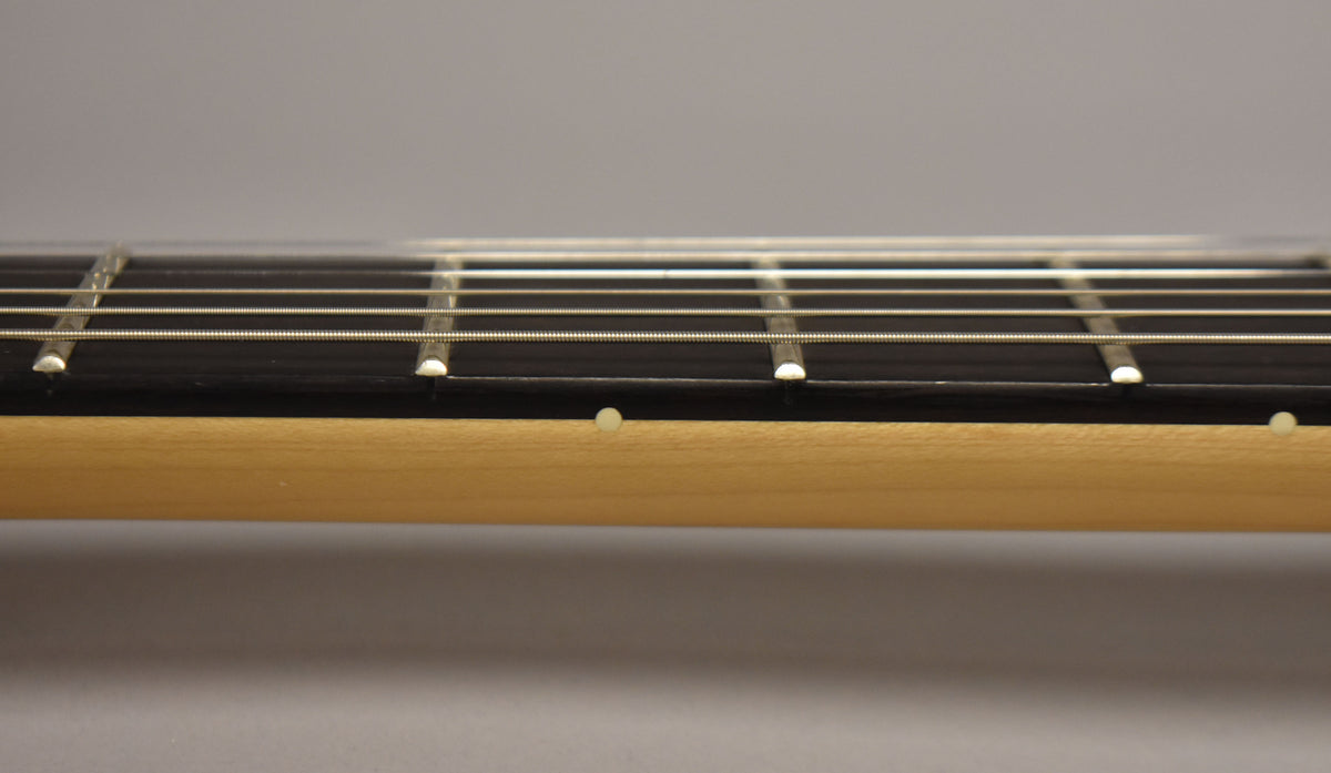 Close-up of the guitar neck, showing the light maple wood, dark fretboard, and white side dot markers.