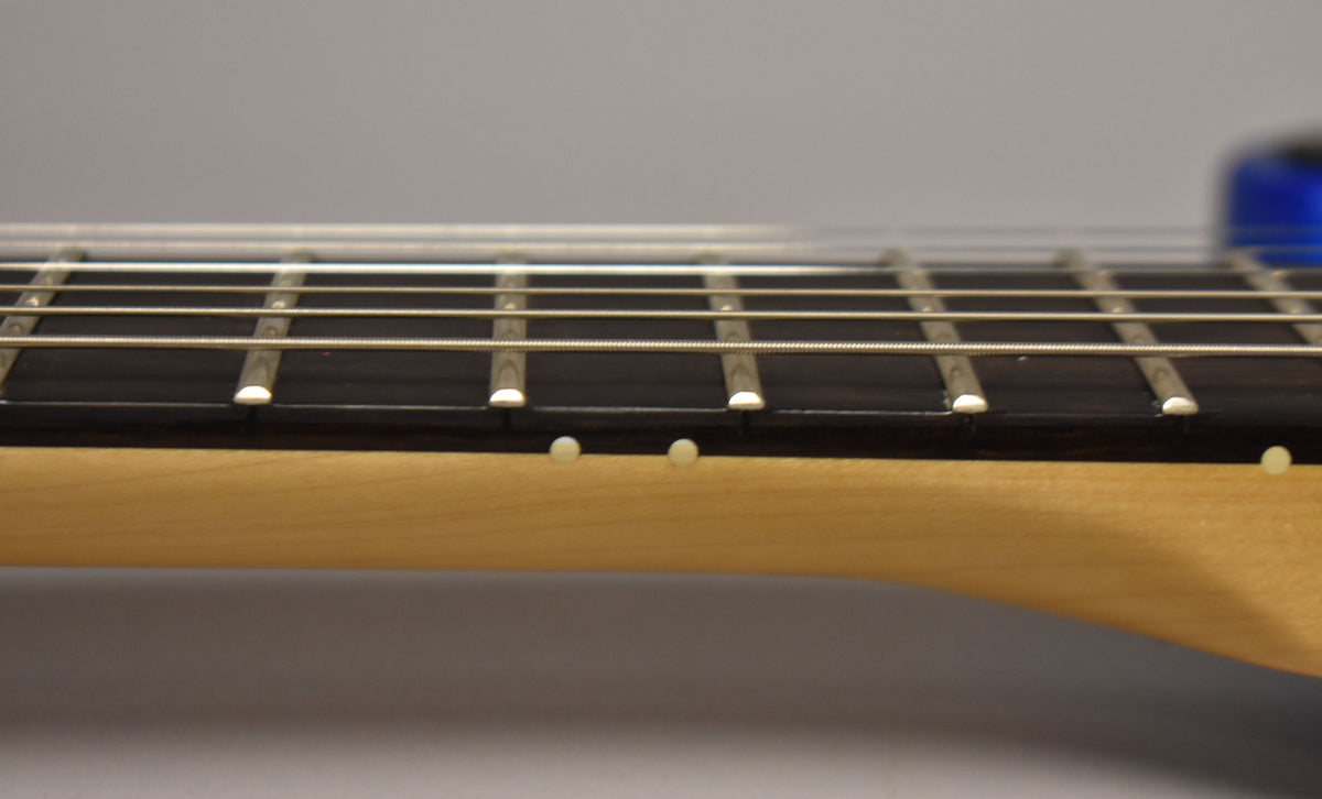 Close-up of the guitar neck from the side, showing the dark fretboard, light frets, and side dot markers on the maple neck.