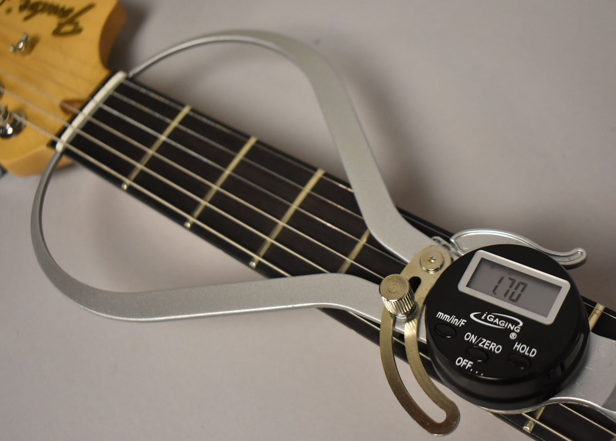 A digital fret rocker tool is clamped to the guitar's dark fretboard, displaying "1.70" on its screen.