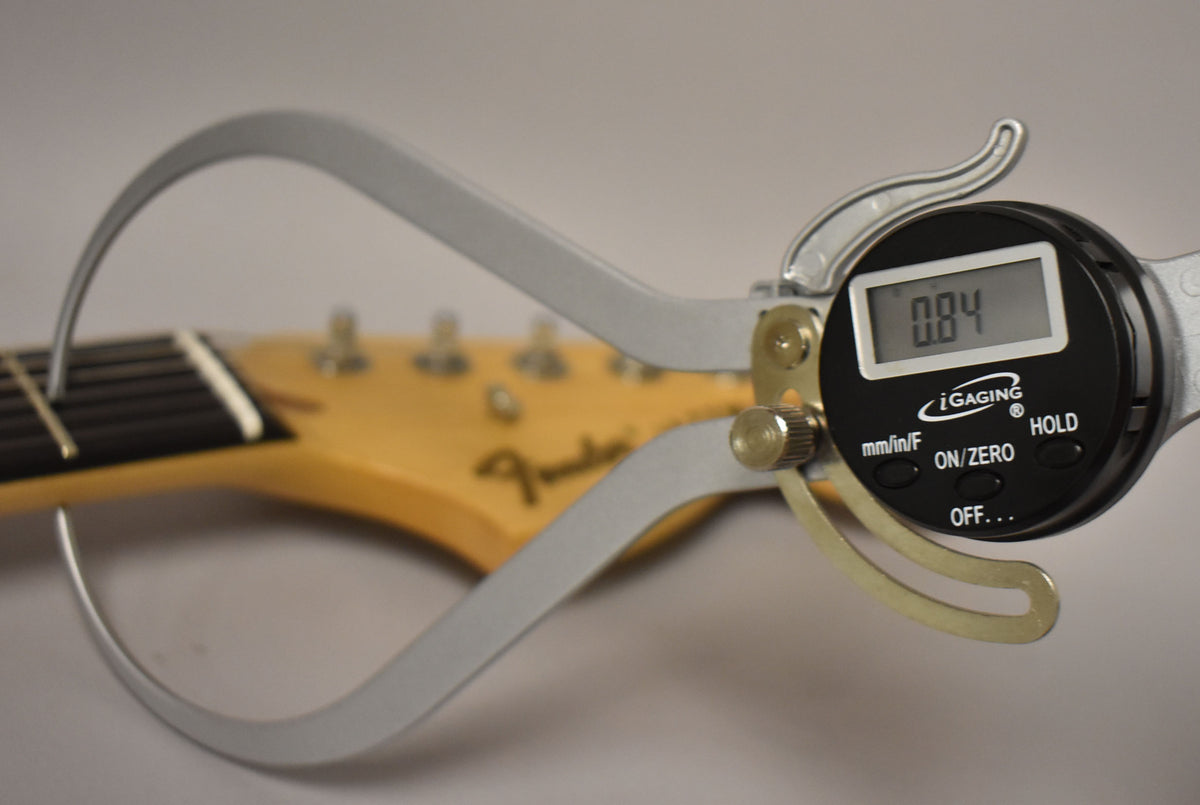 A digital caliper measures the nut height of the guitar neck, showing "0.84" on its screen.