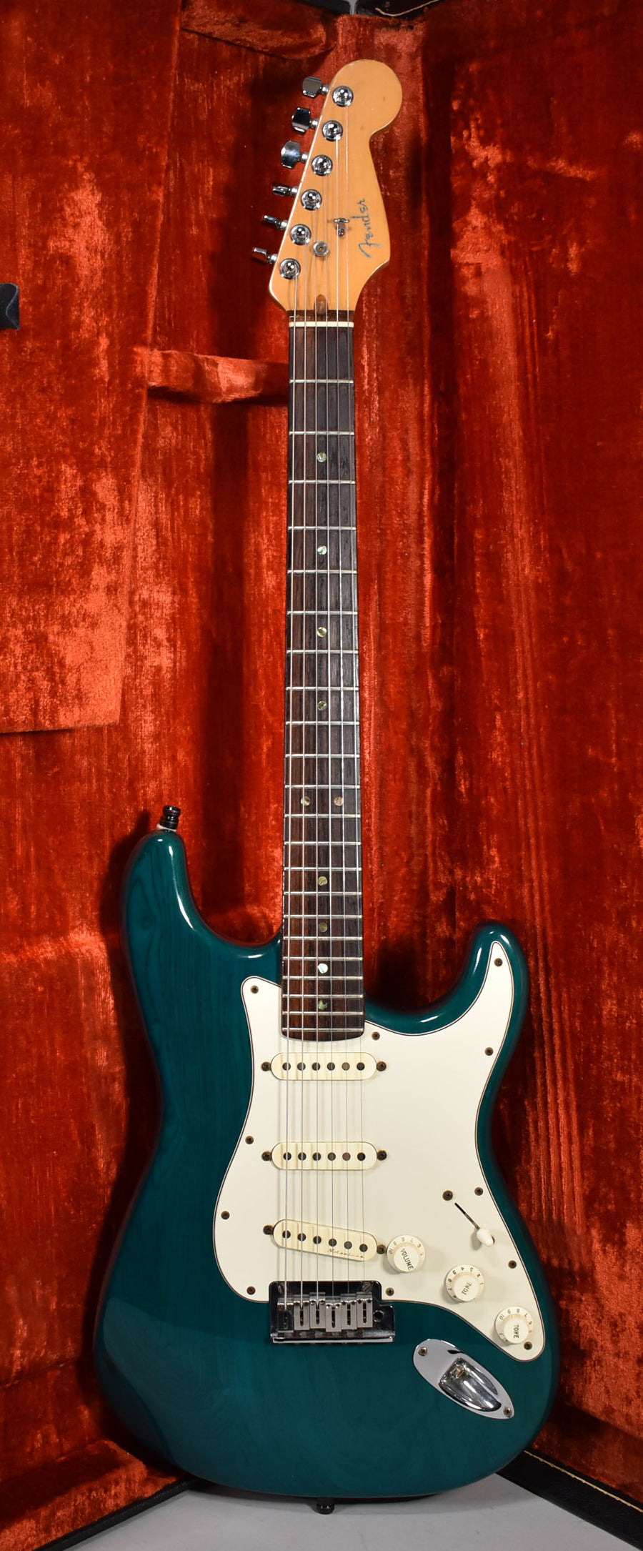 Full-length view of a transparent teal Stratocaster with a white pickguard, three cream pickups, and chrome hardware, resting in a red velvet case.