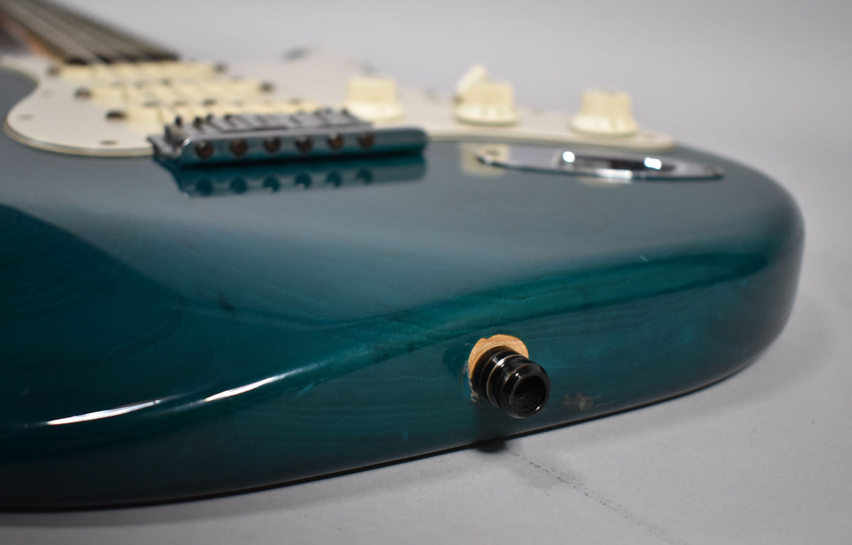 Close-up of the guitar's lower bout, showing the transparent teal finish, output jack, and light wear on the body.