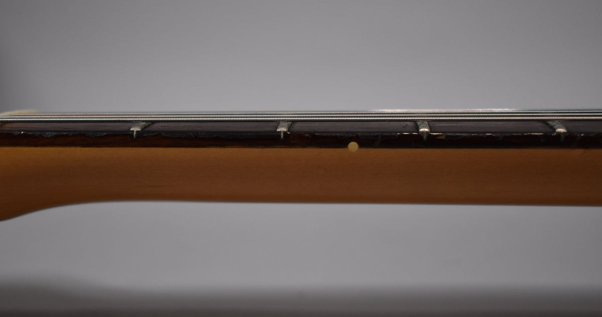 Close-up of the guitar's neck and fretboard, showing a light brown neck, dark fretboard, and a circular fret marker.