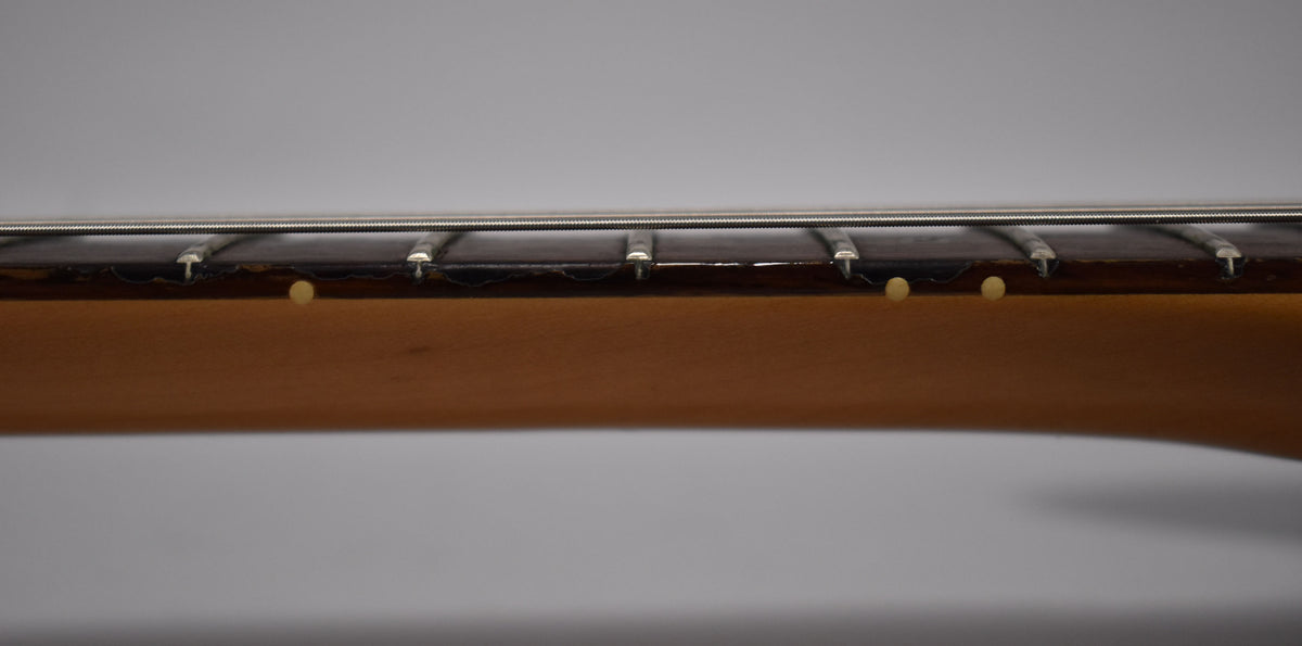 Close-up of the guitar's neck from the side, showing the dark fretboard with light dot inlays and some wear along the edge.