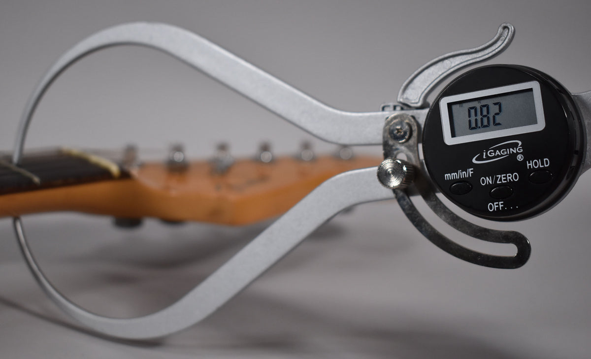 A digital caliper measures the guitar's neck thickness at 0.82 inches, with the headstock and tuners blurred in the background.