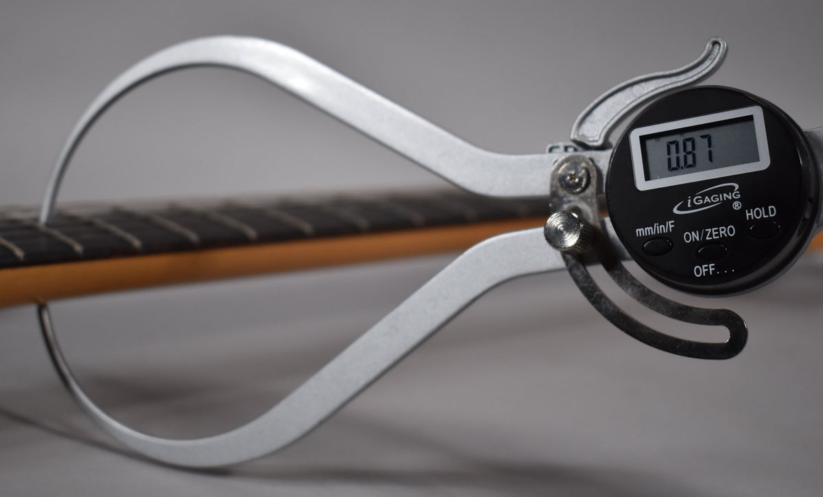 A digital fret height gauge measures a fret on the dark rosewood fingerboard of the guitar's maple neck.