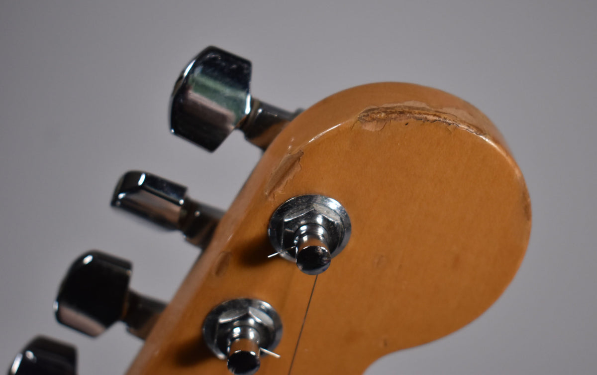 Close-up of the guitar's headstock from the back, showing a large chip in the finish near the top edge and chrome tuners.