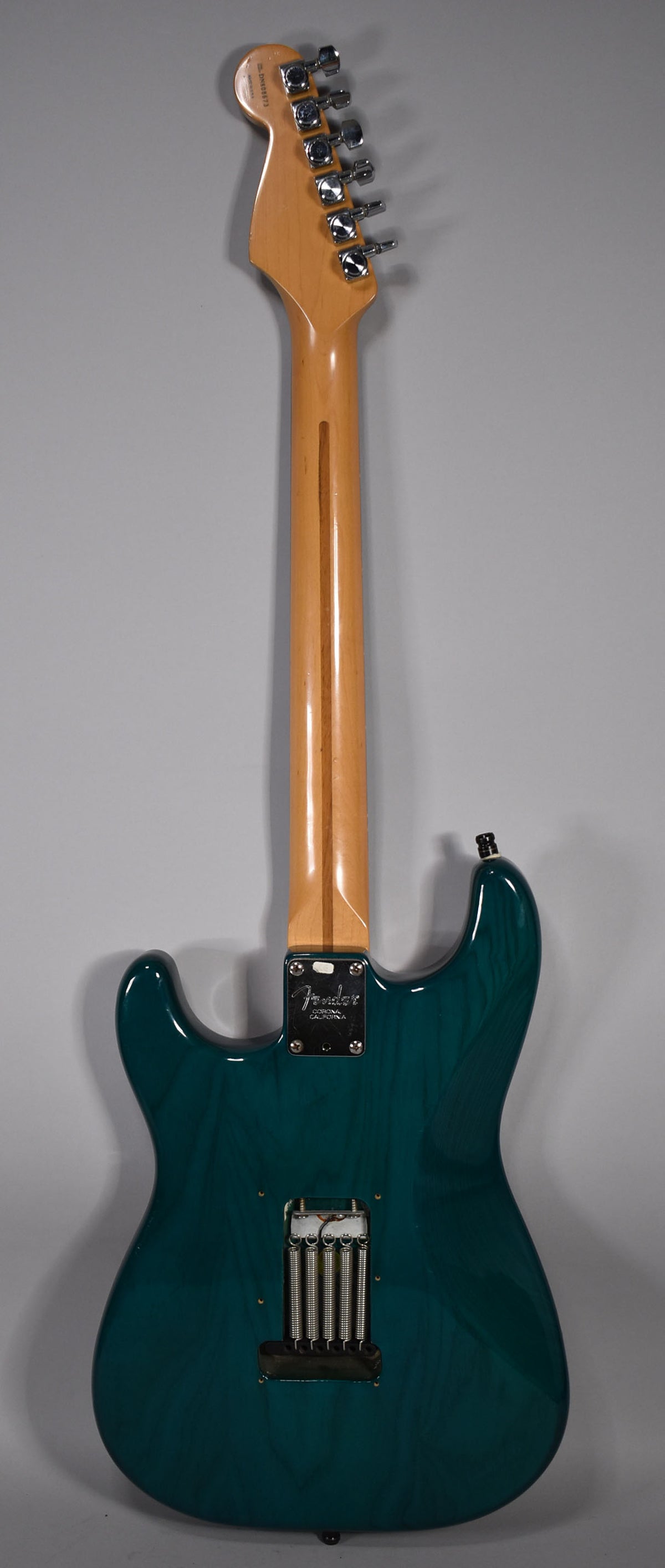 The guitar's back, showing a transparent teal finish with visible wood grain, a maple neck, and the tremolo spring cavity.