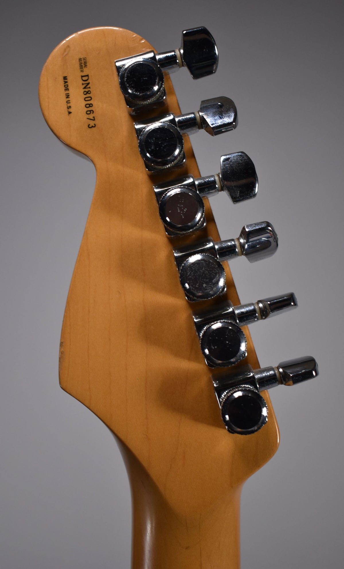 The back of a light brown maple headstock with six chrome tuners, showing light wear and a small chip on the top edge.
