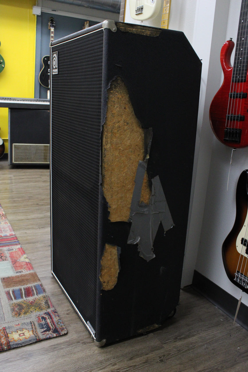 The tall black speaker cabinet is angled, revealing a large tear in the tolex on the right side, exposing the wood underneath.